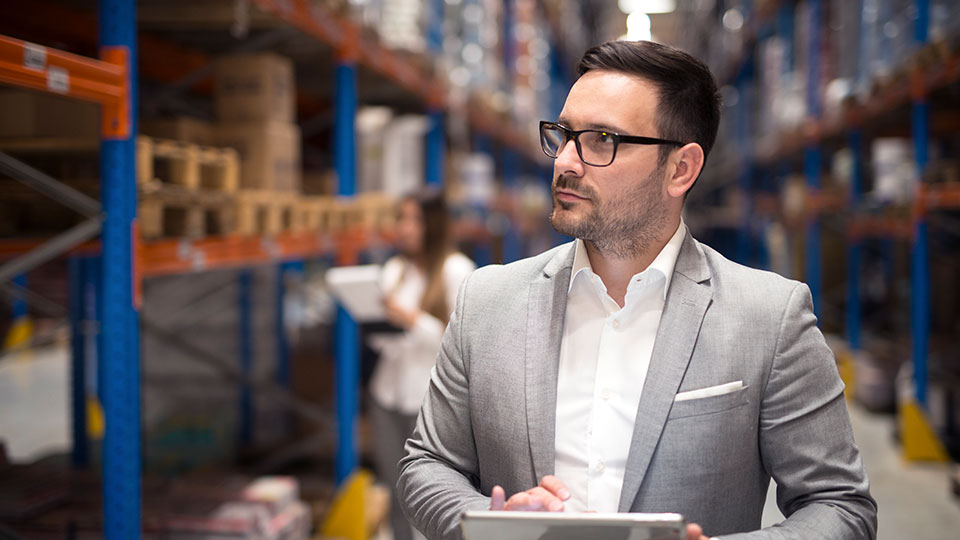Mann mit Tablet inspiziert Regale in einem Warenlager.