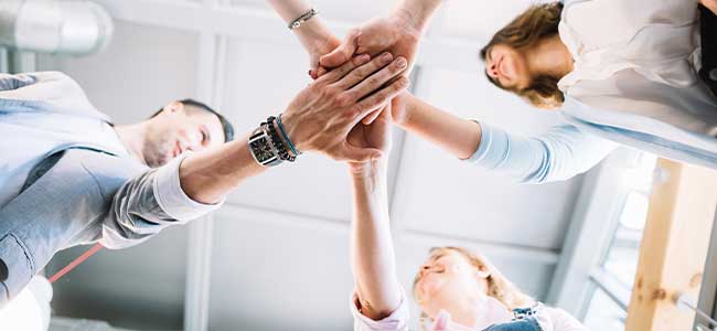 Vier Teammitglieder, die ihre Hände in einer Geste der Einheit und Teamarbeit übereinanderlegen.