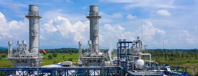 Moderne Industrie 4.0 - Industrieanlage mit Dampftürmen und Rohrsystemen in grüner Landschaft unter blauem Himmel – Symbol für Energieproduktion und industrielle Effizienz.