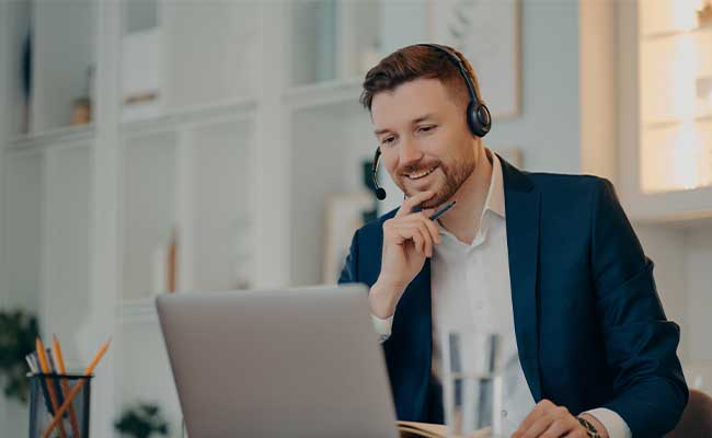 Freundlicher Mitarbeiter mit Headset im Gespräch am Schreibtisch.