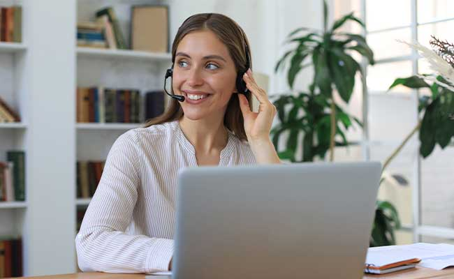 Freundliche Mitarbeiterin mit Headset im Gespräch am Schreibtisch.