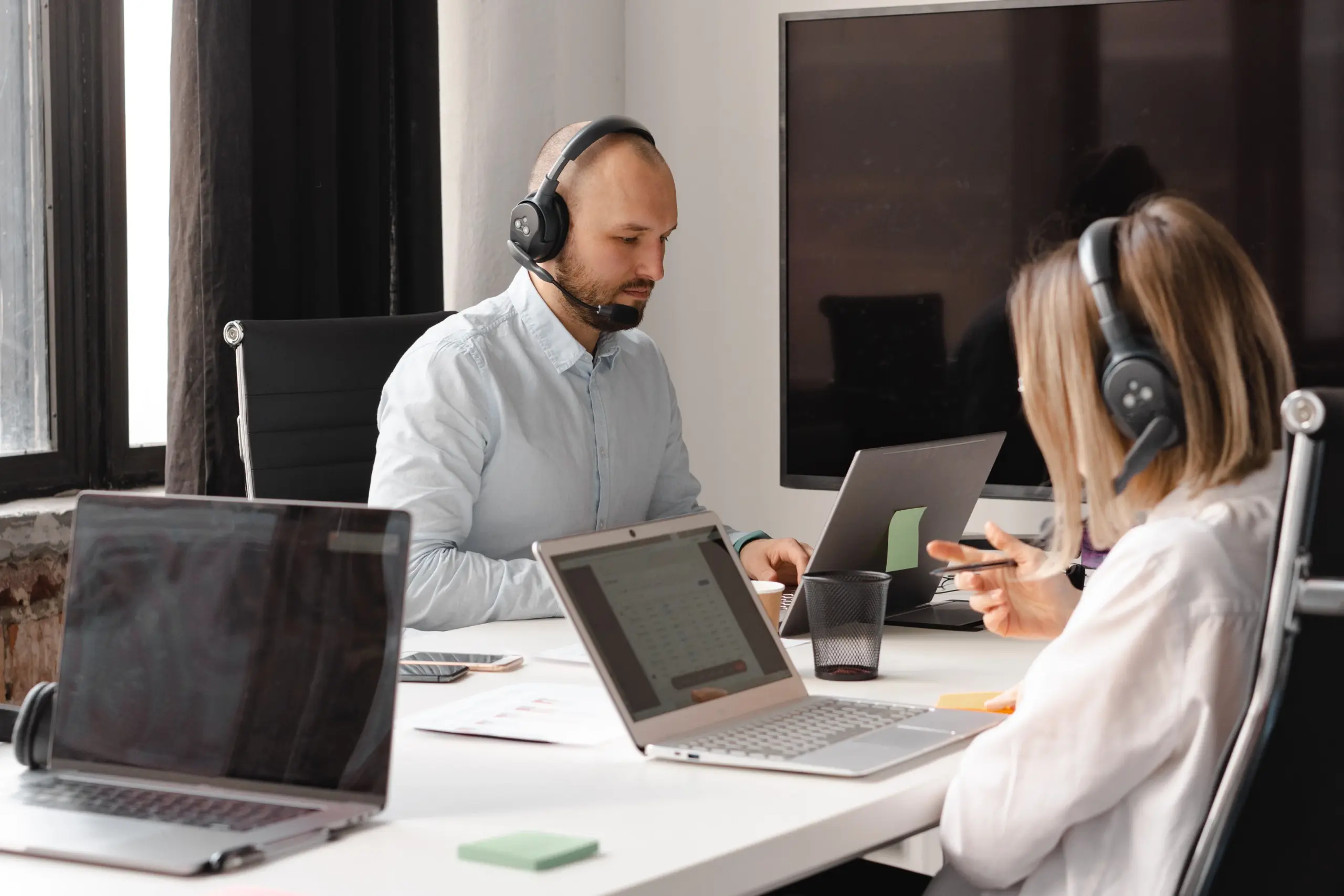 Zwei Mitarbeitende mit Headsets arbeiten im Büro an Laptops und besprechen eine Support-Anfrage